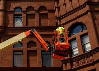 A worker moves a skylift as construction crews work on masonry upgrades on Crouse College. Photo taken July 18, 2017