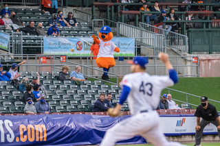 Jerad Eickhoff pitches the ball  while Scooch, the team's mascot, greets fans in the stands. 